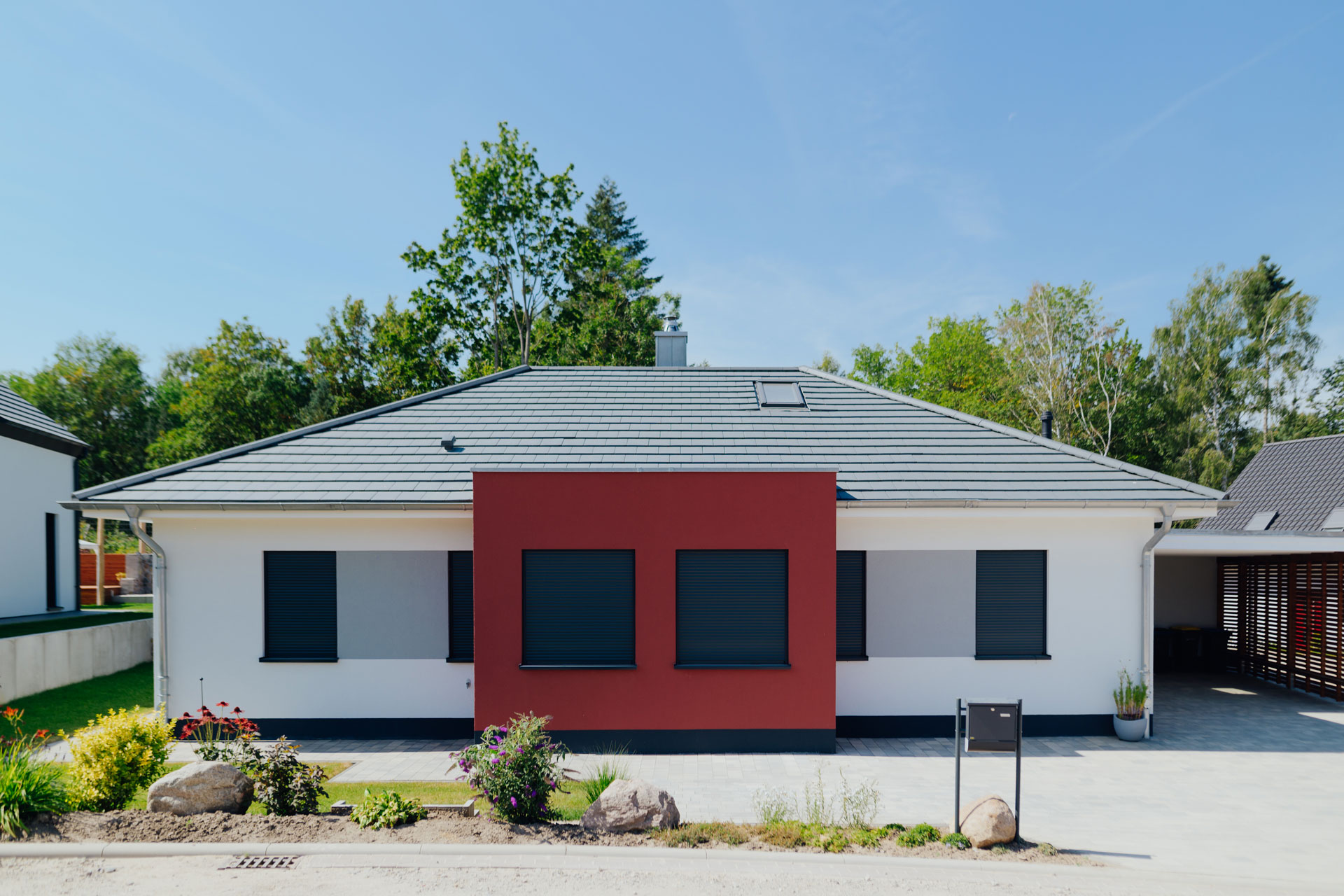 Ein weißes Einfamilienhaus hat einen roten Farbakzent an einen zentralen Vorbau.