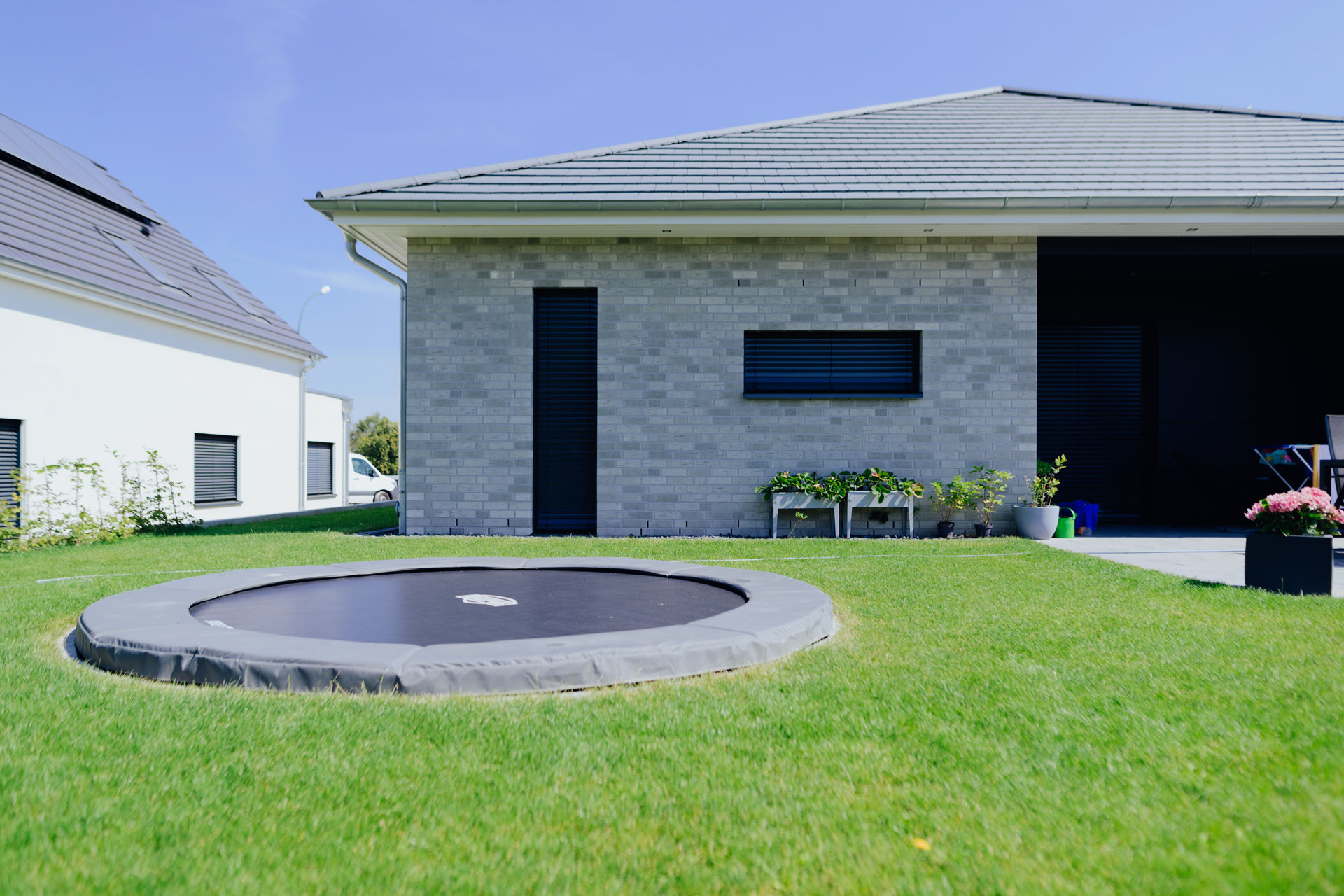 Auf einem gepflegten kurzen Rasen ist ein rundes Bodentrampolin. Dahinter steht ein Einfamilienhaus.