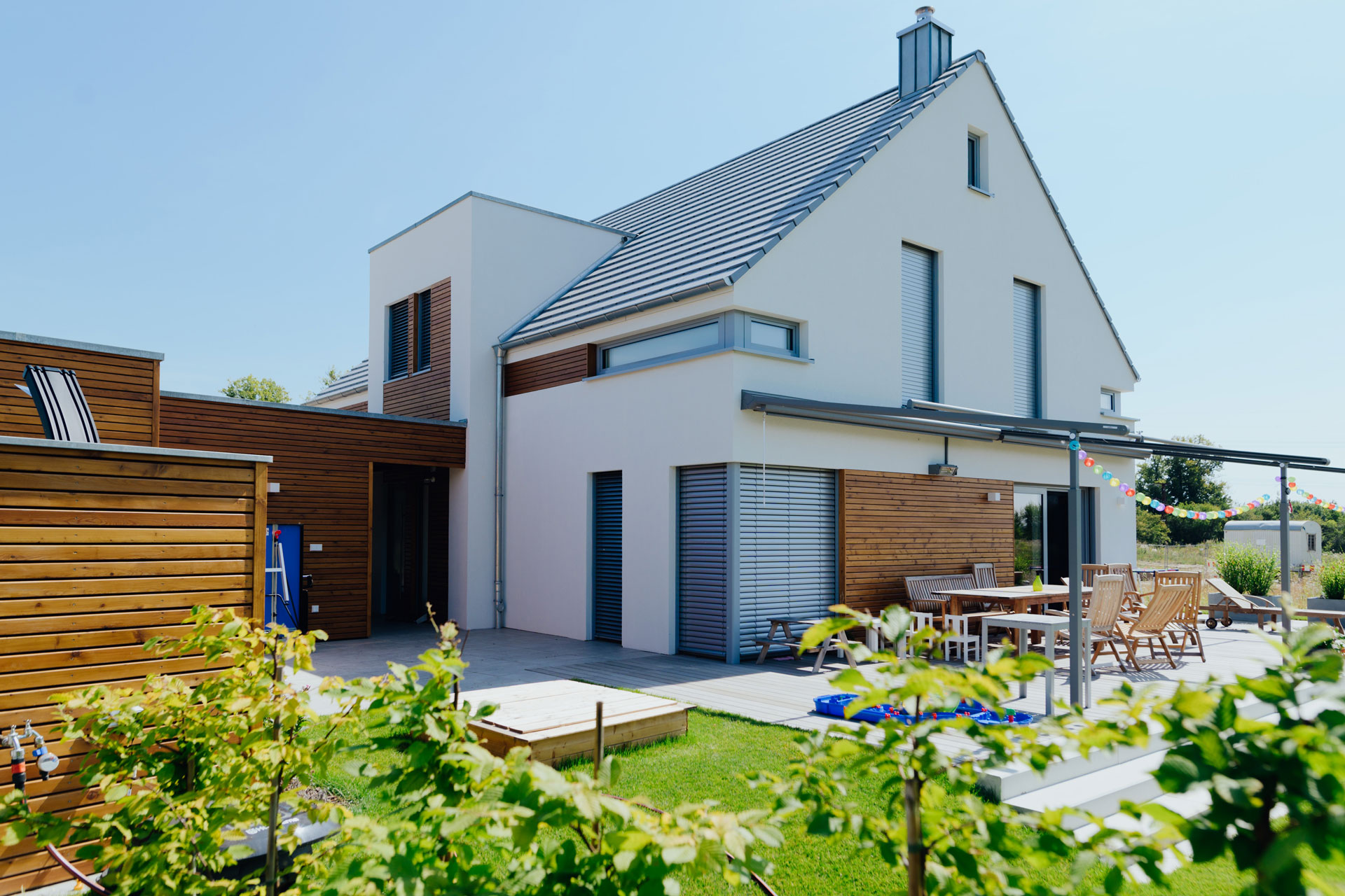 Totalaufnahme eines Einfamilienhauses mit Spitzdach. Vor dem Terrassenbereich ist der Garten.