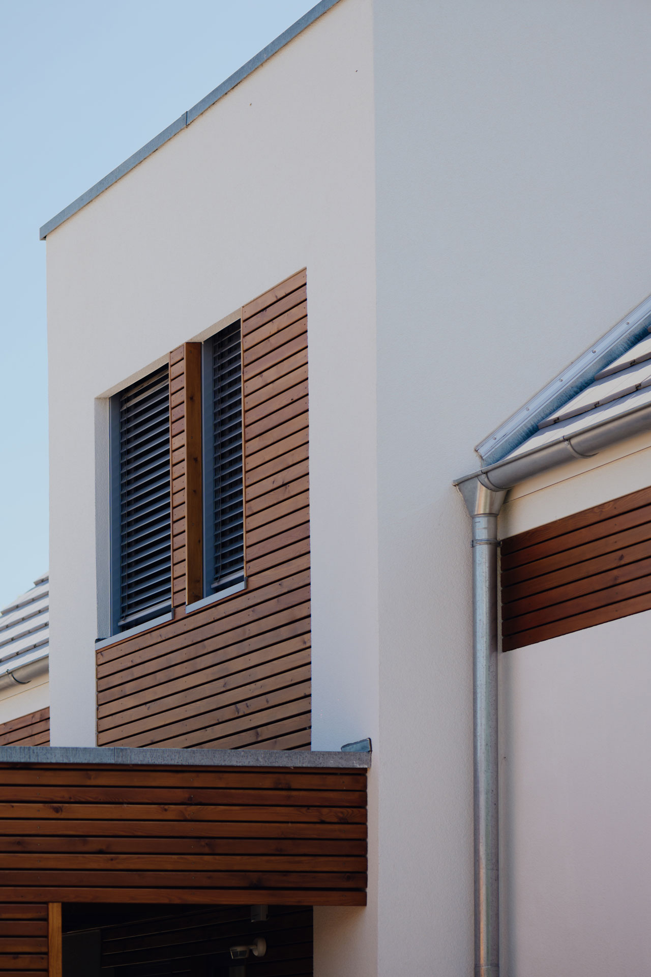 Eine Detailaufnahme zeigt zwei Fenster im weißen Mauerwerk. Akzenten aus Holz umgeben diese seitlich.
