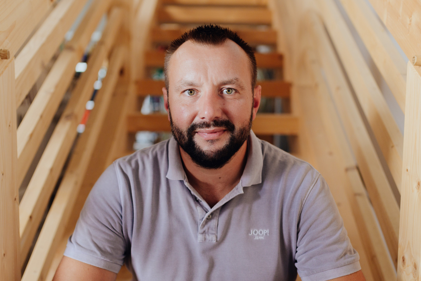Stefan Müller sitzt auf einer Holztreppe. Er schaut freundlich in die Kamera.