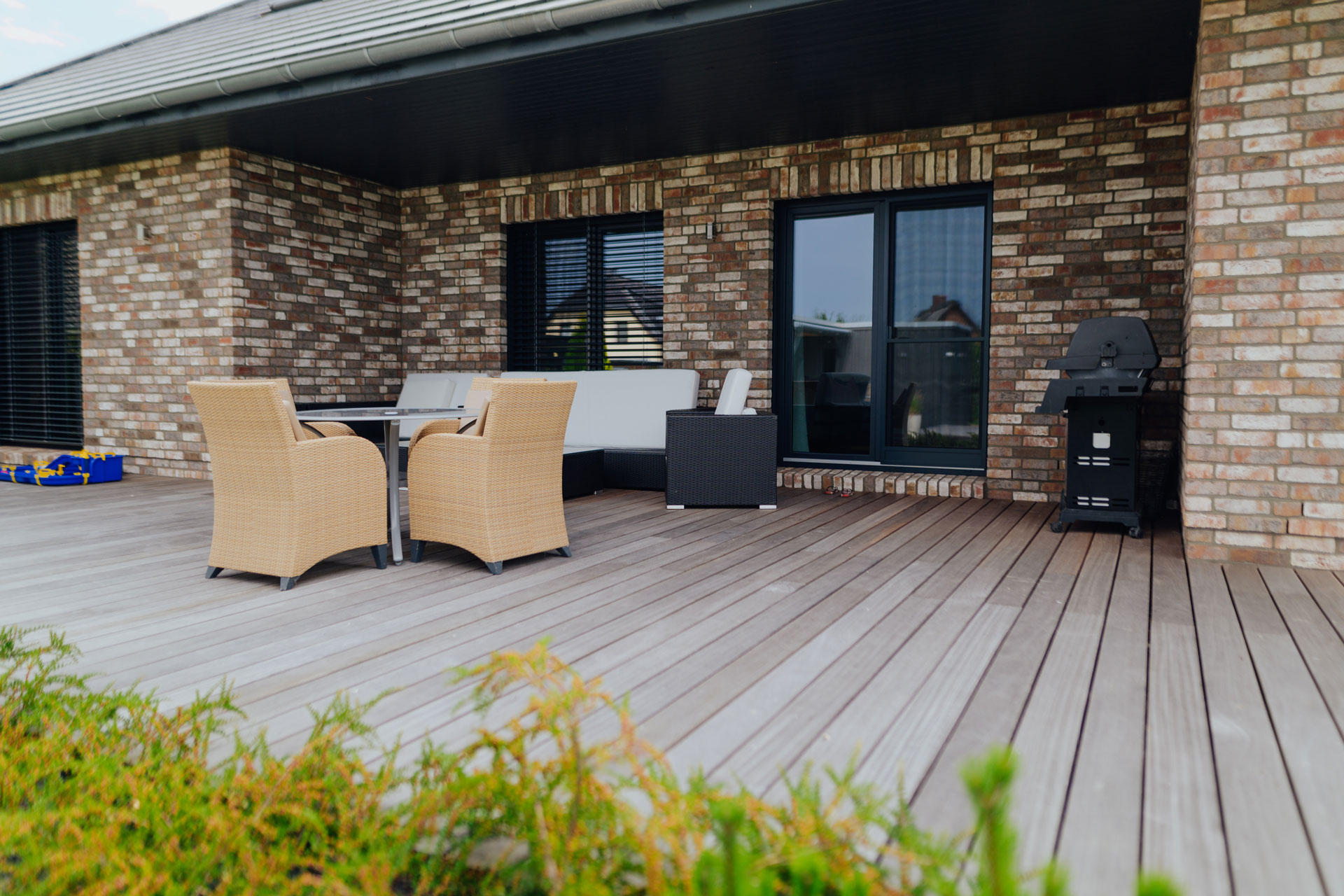 Auf einer Terrasse mit Holzboden befindet sich ein Sitzbereich und Grill.