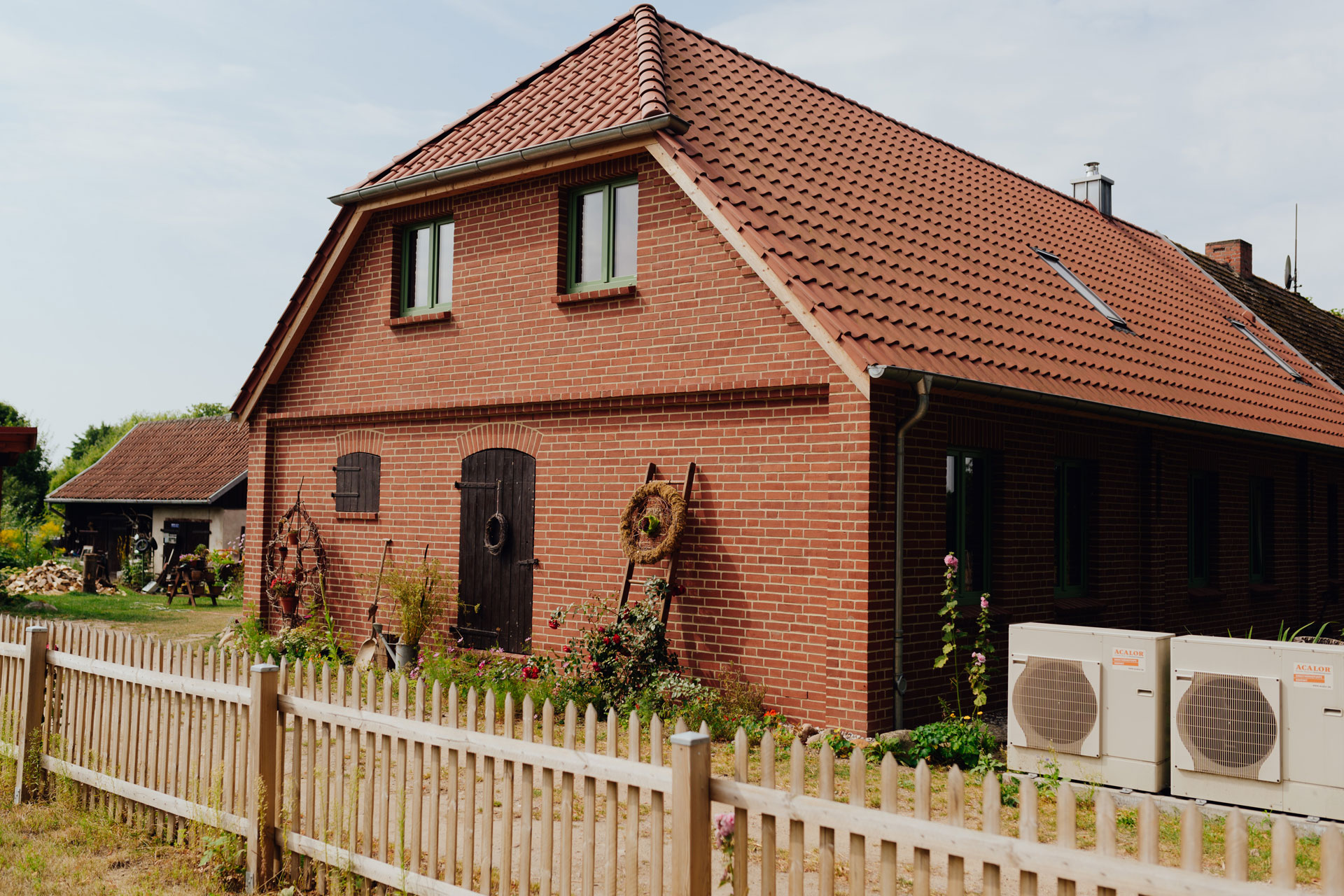 Ein rotgemauerten Einfamilienhaus ist von einem Holzzaun umgeben.