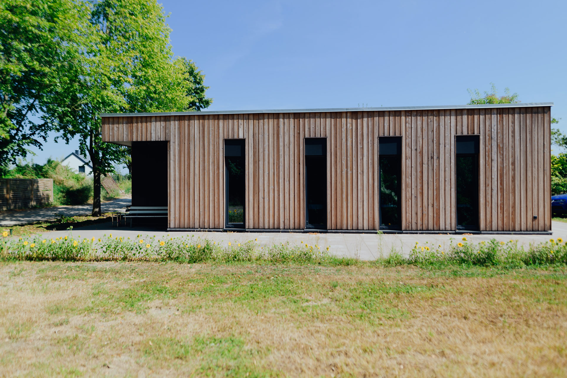 Eine Schuppenanlage aus Holz hat mehrere schmale Fenster. Die Sommersonne scheint.