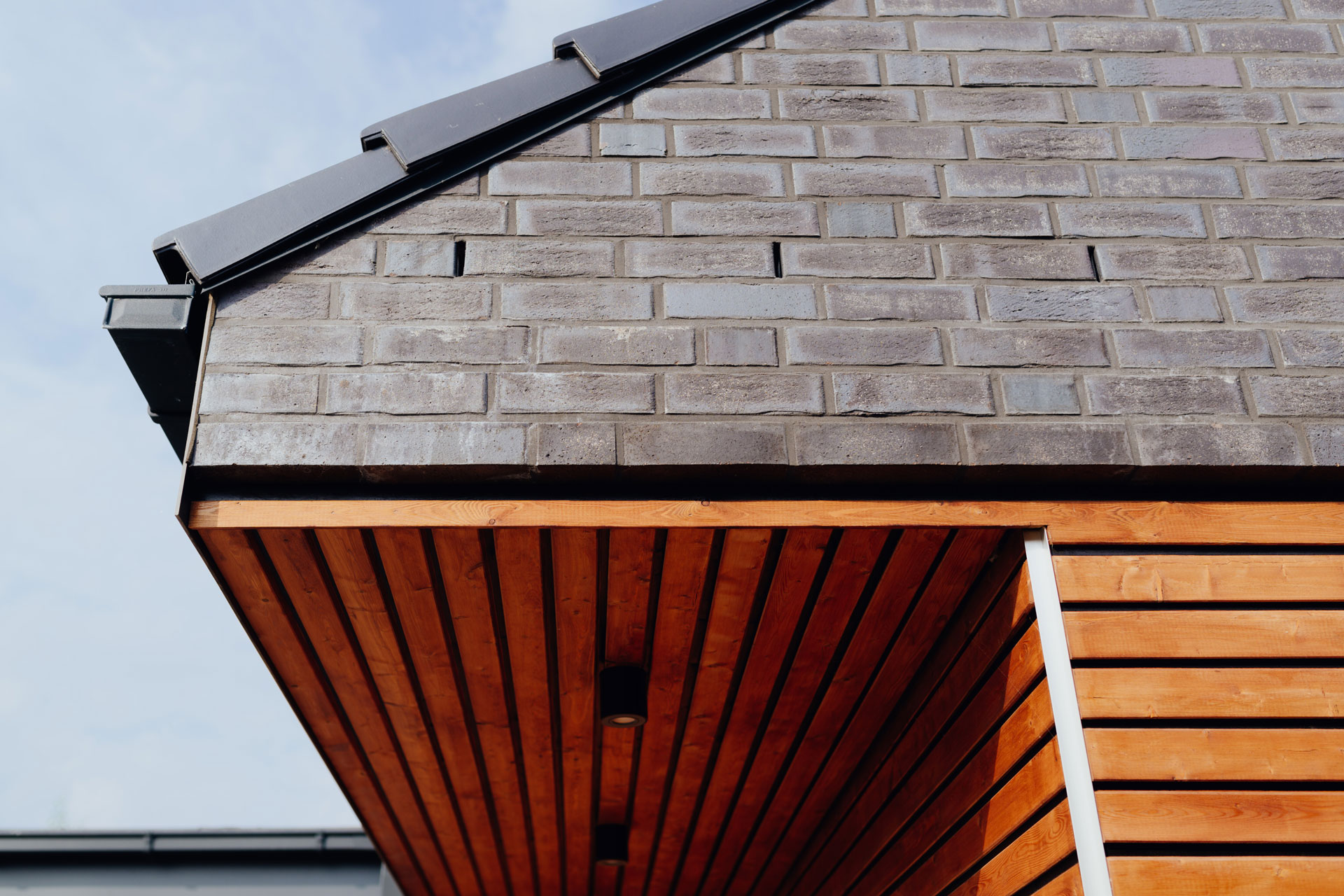 Hellbraunes Holz eines Carports grenzt an schiefergraues Mauerwerk an.