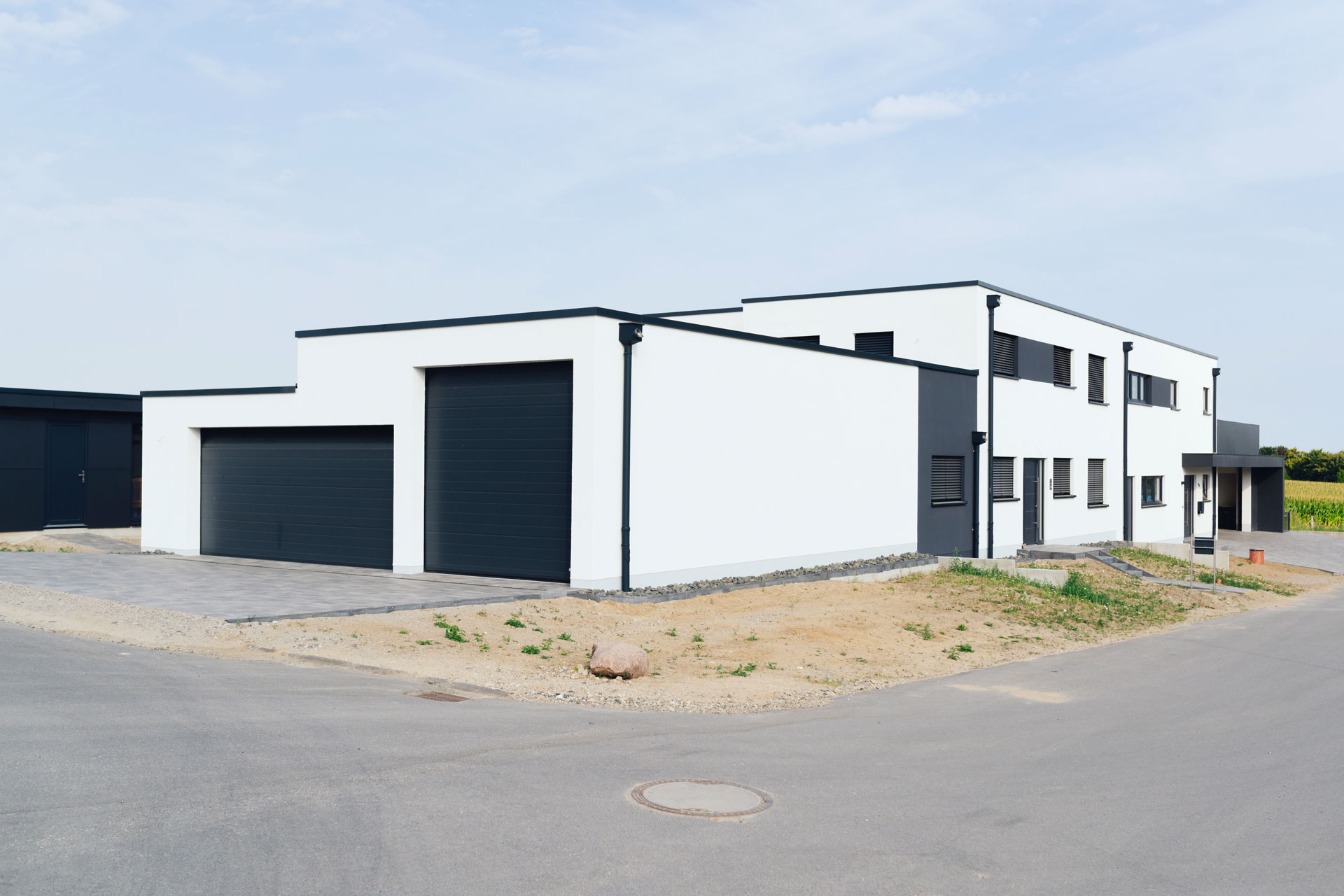 An einen großen Carport grenzt ein modernes Doppelhaus an. Die Fassade ist weiß.