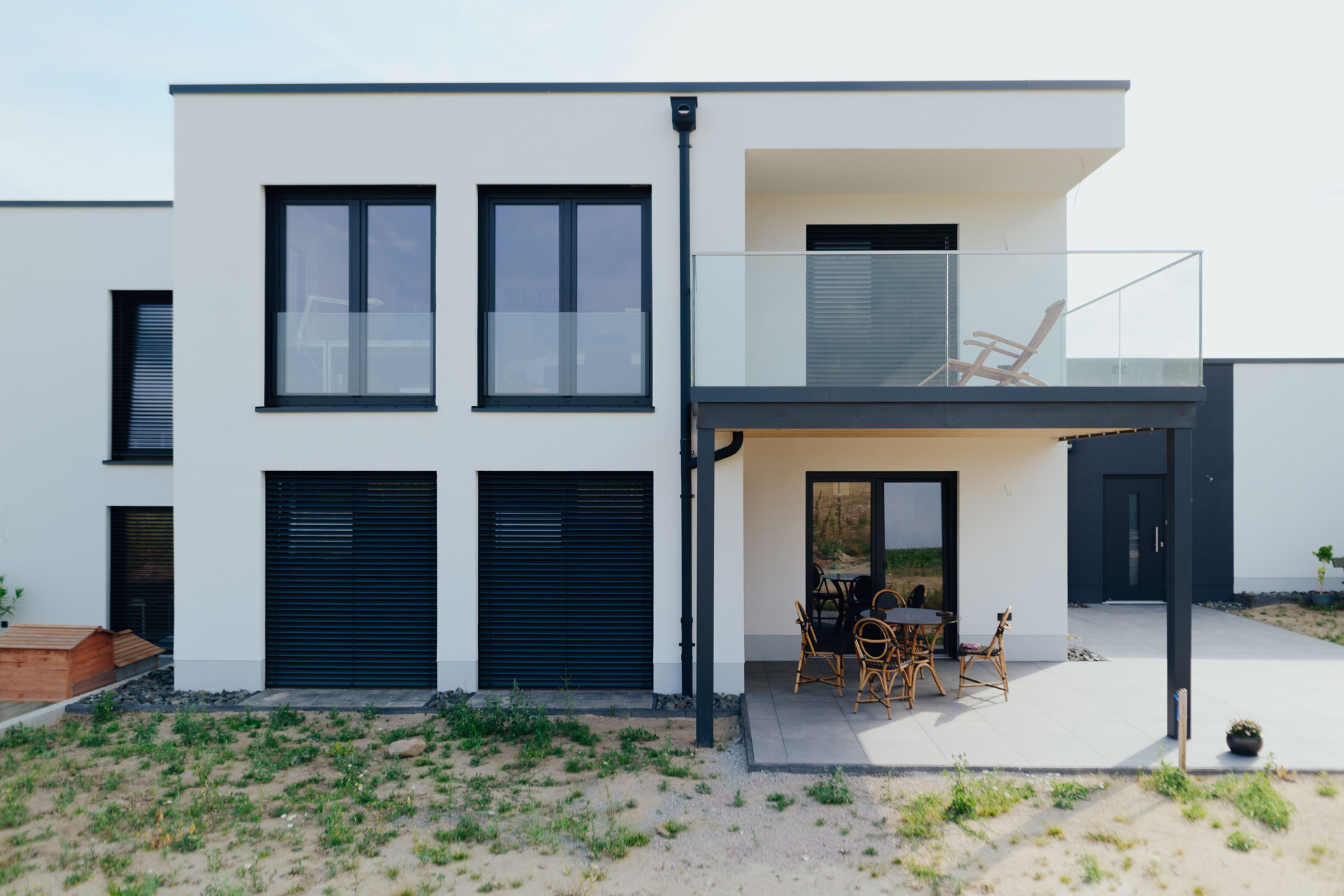 Auf einer Terrasse eines modernen Doppelhauses steht ein Tisch und fünf Stühle.