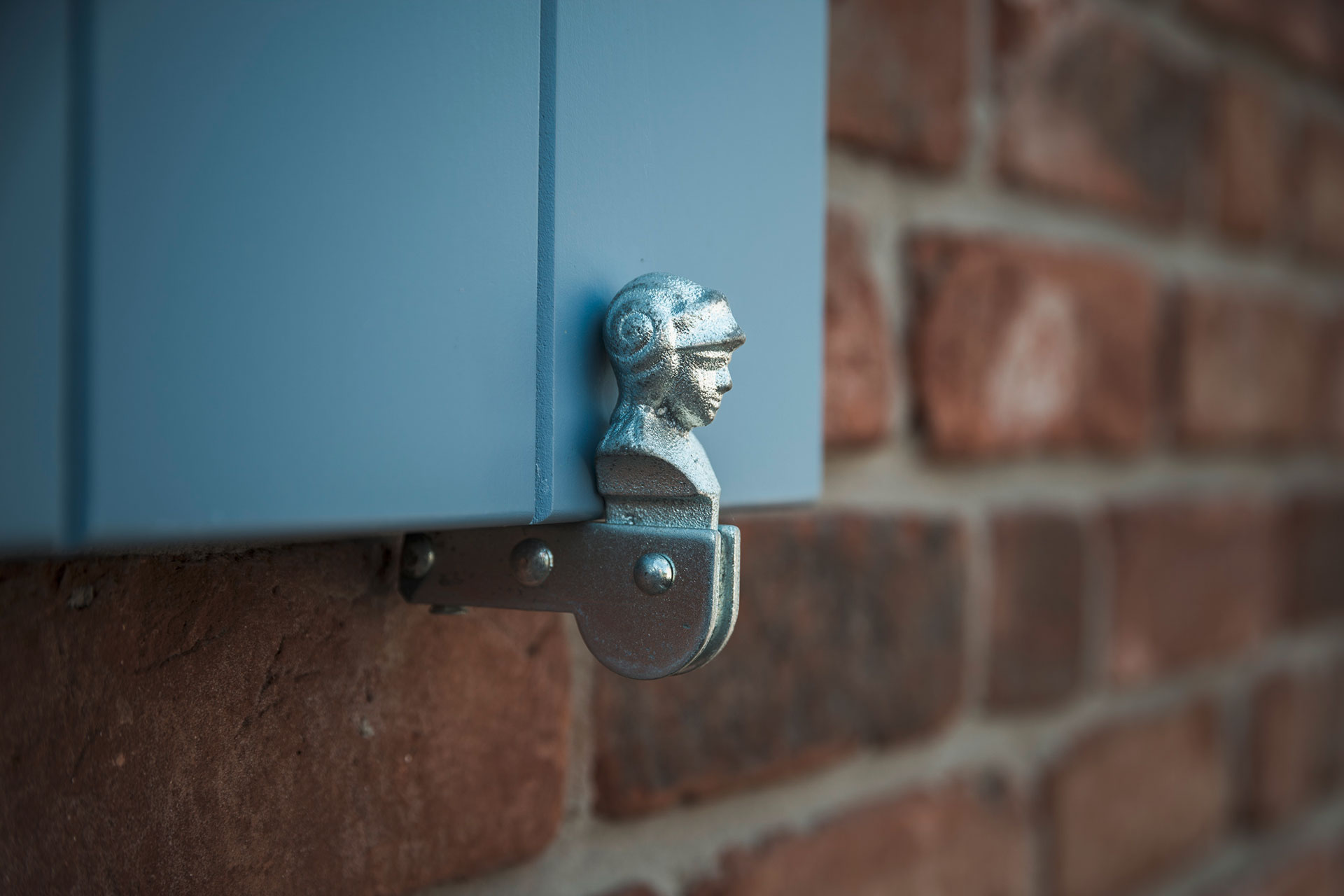 An einem blaugestrichenen Fensterladen ist ein gusseiserner Zierscharnier. Es ist ein Kopf eines Mannes.