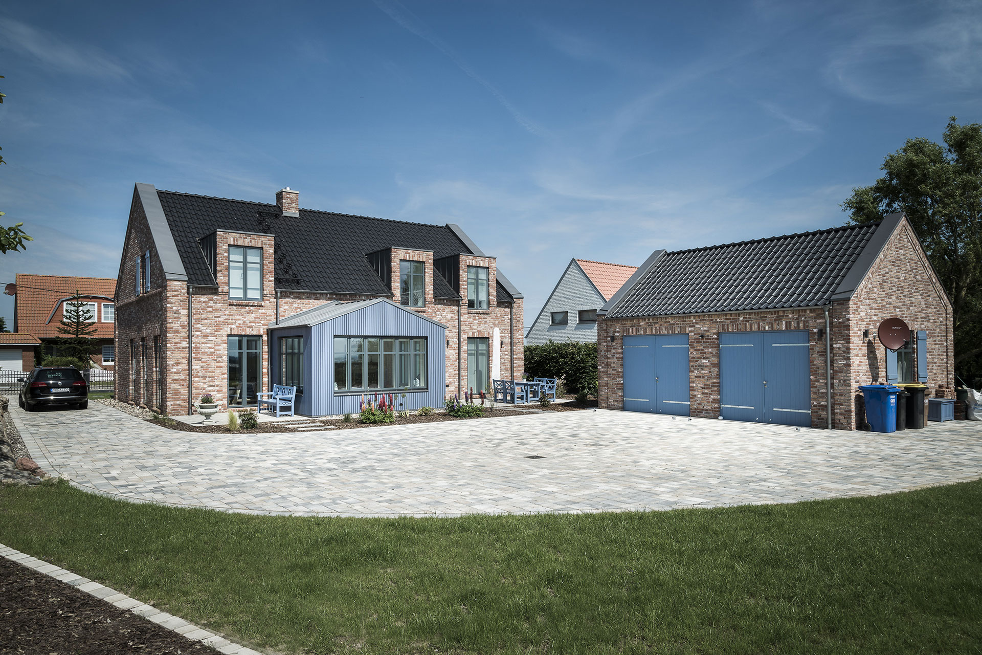 Ein rotgemauertes Einfamilienhaus hat einen blaugestrichenen Wintergarten und einen großen Garagenbau.