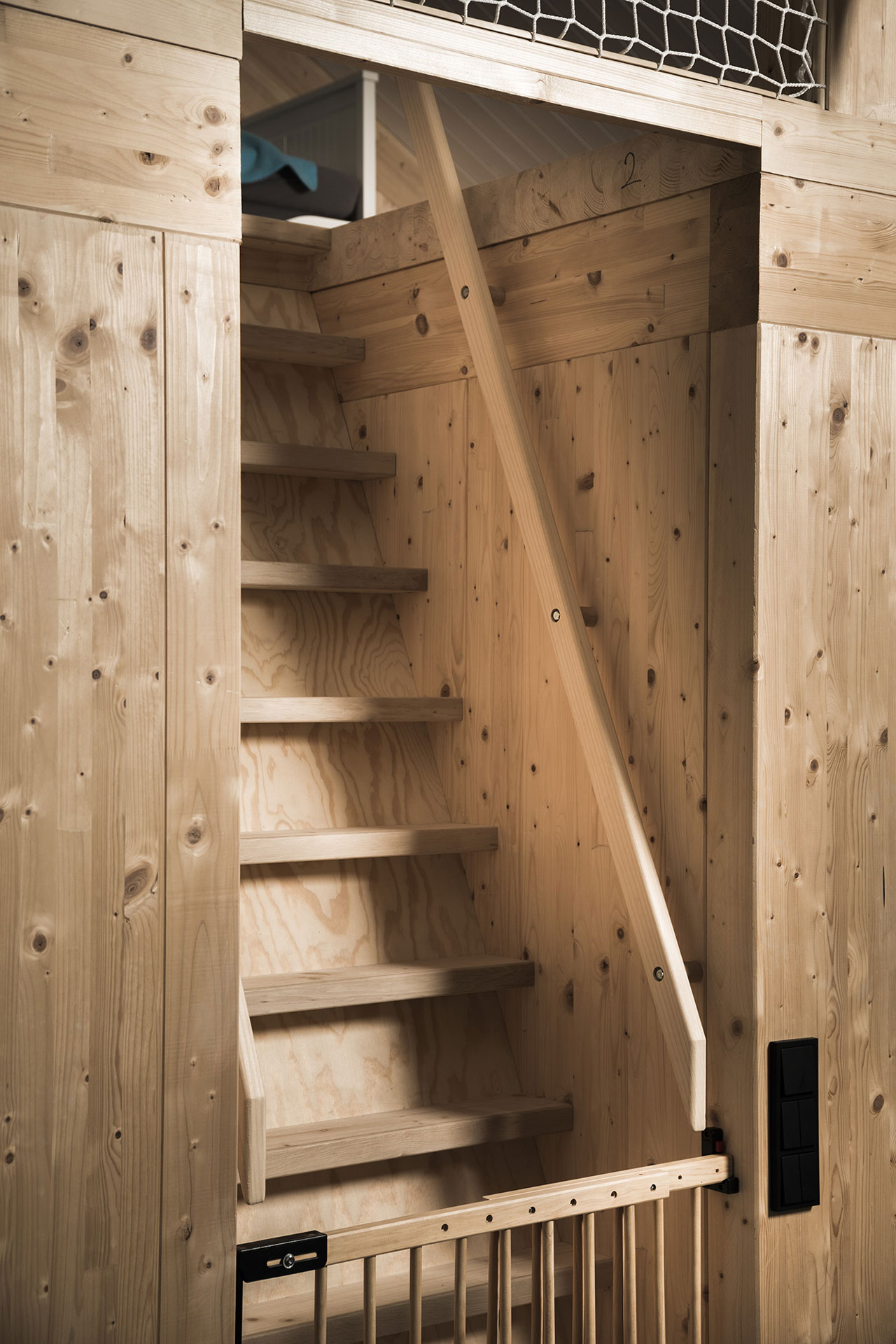 Eine steile Holztreppe führt ins Dachgeschoß. Das Holz ist hellbraun.
