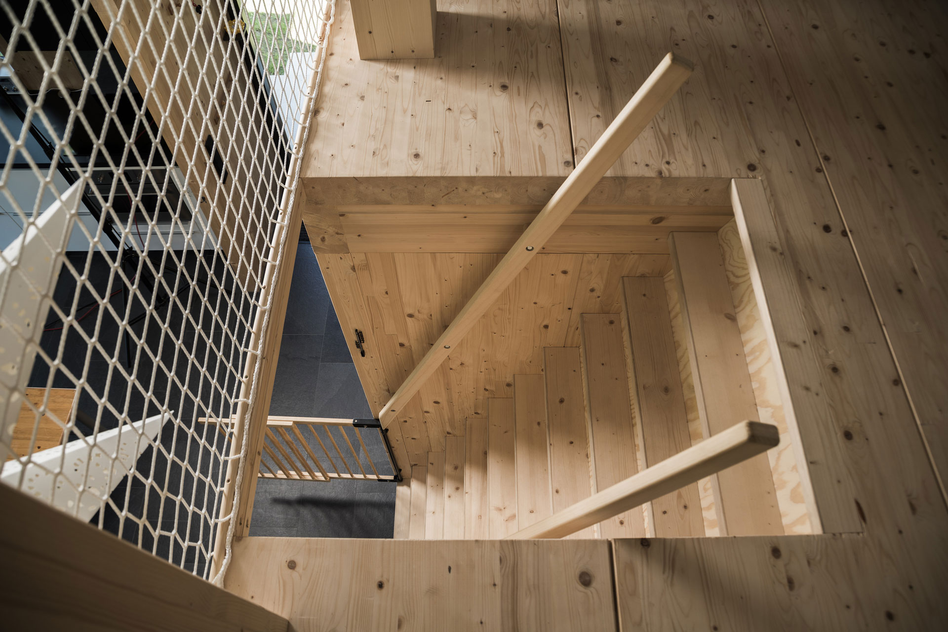 Man blickt an einer Holztreppe herunter. Das Holz ist hellbraun.