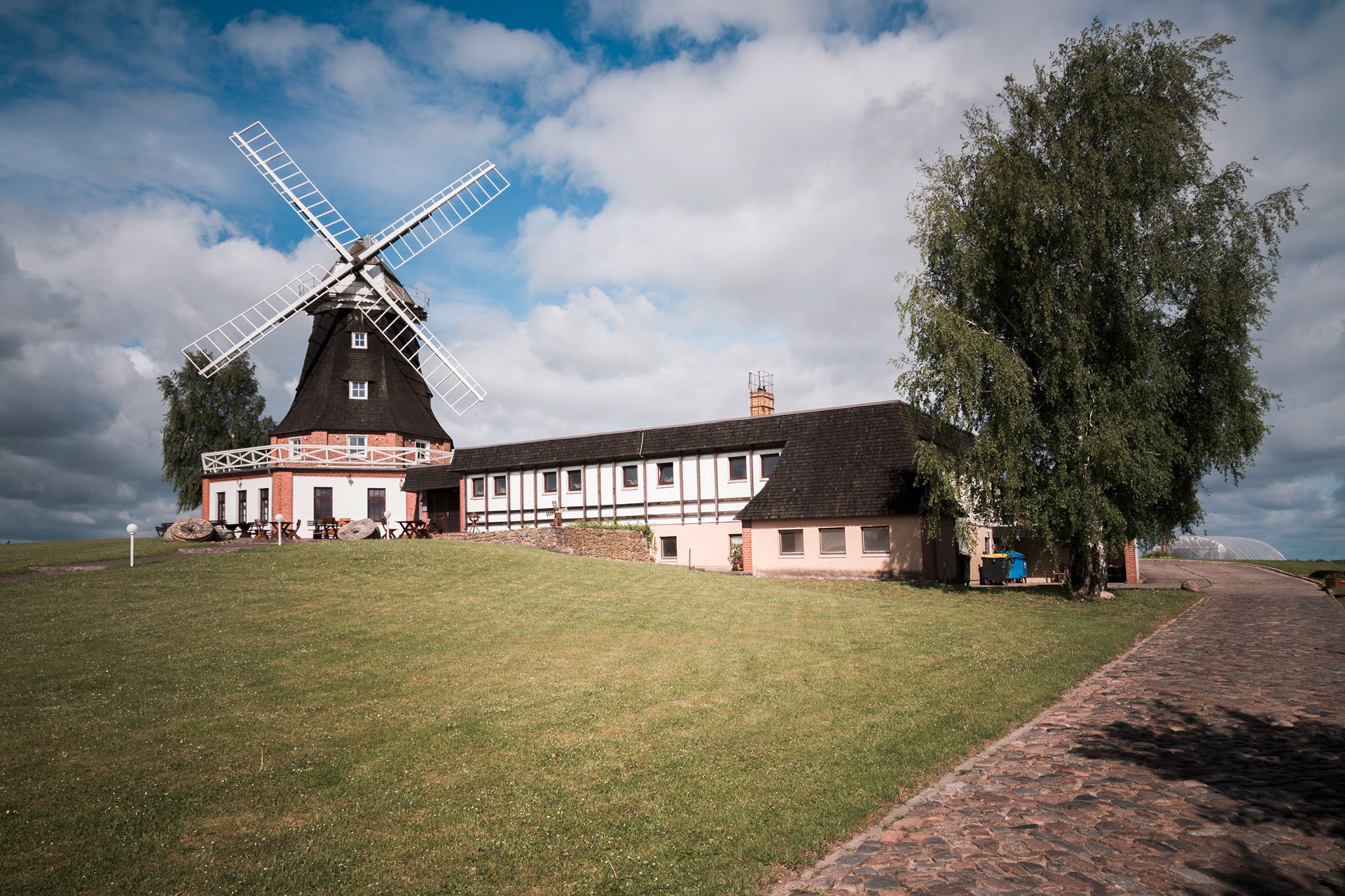 Auf einer weitläufigen Rasenfläche steht eine alte Mühle. Am blauen Himmel sind viele Wolken.