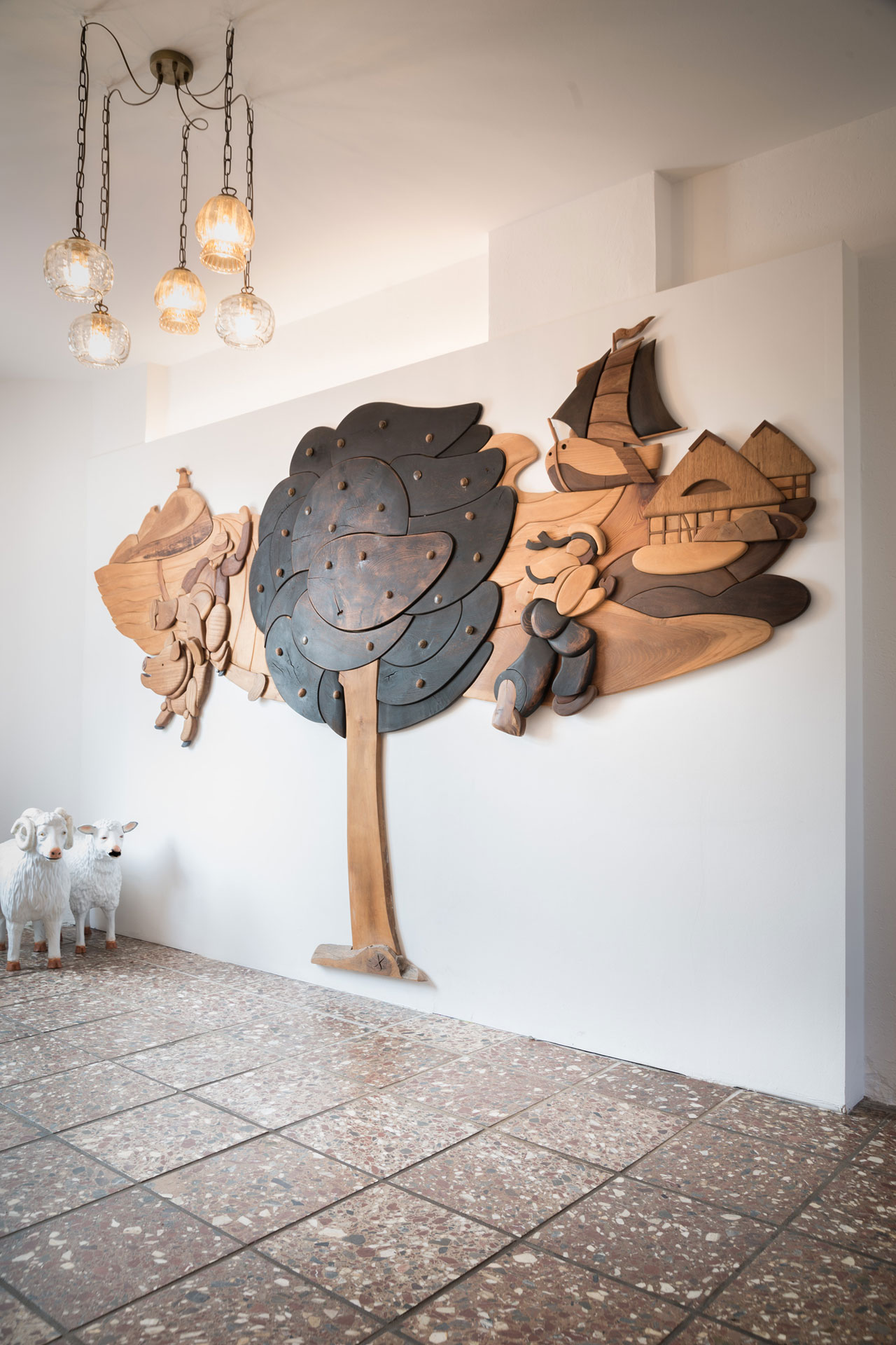 Eine Wand hat ein dekoratives Wandelement aus Holz. Es sind ein Baum, Häuser und Boote erkennbar.