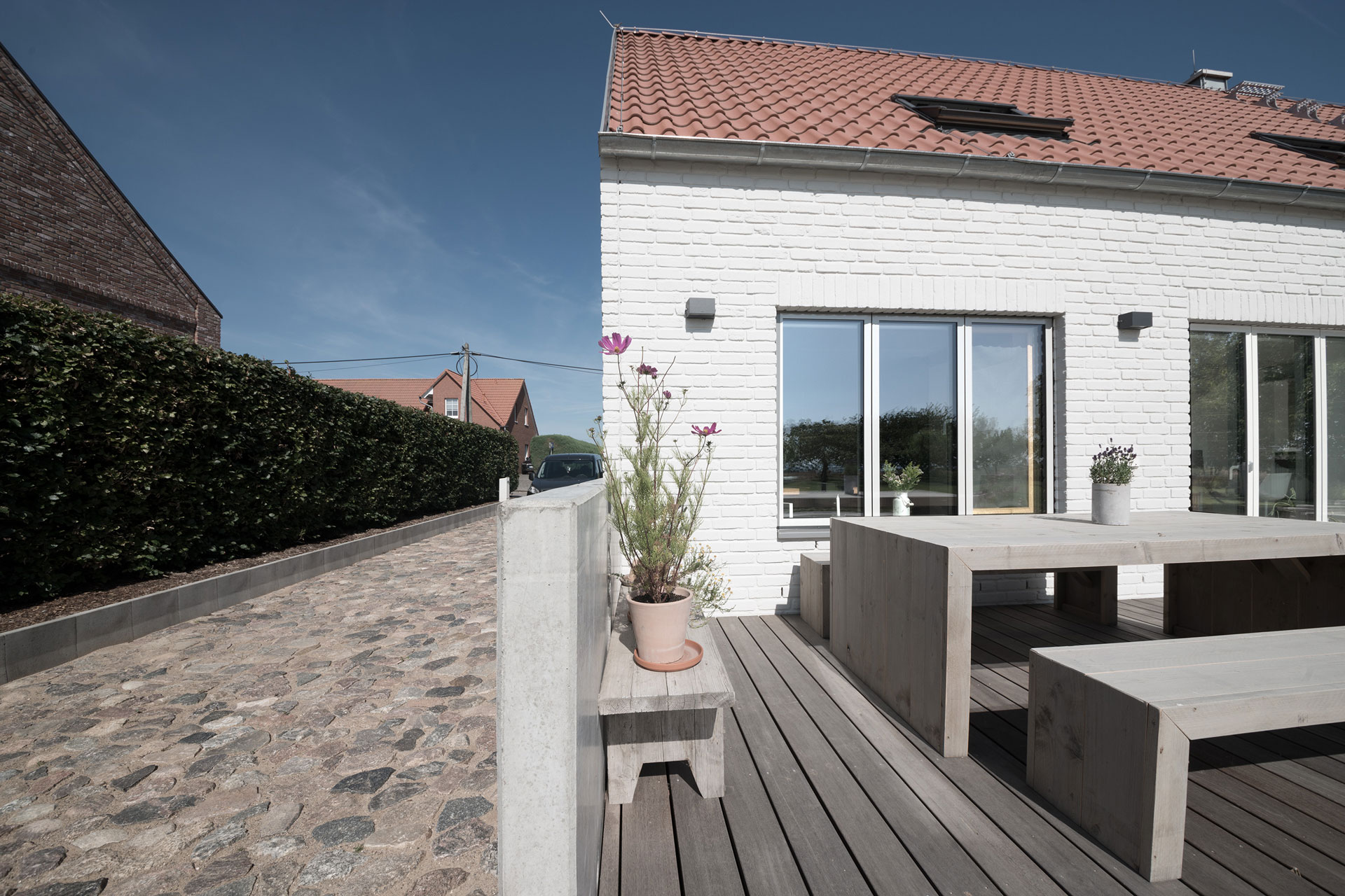 Neben einer Terrasse aus Holz grenzt ein steingepflasterter Weg an. Die Sonne scheint.