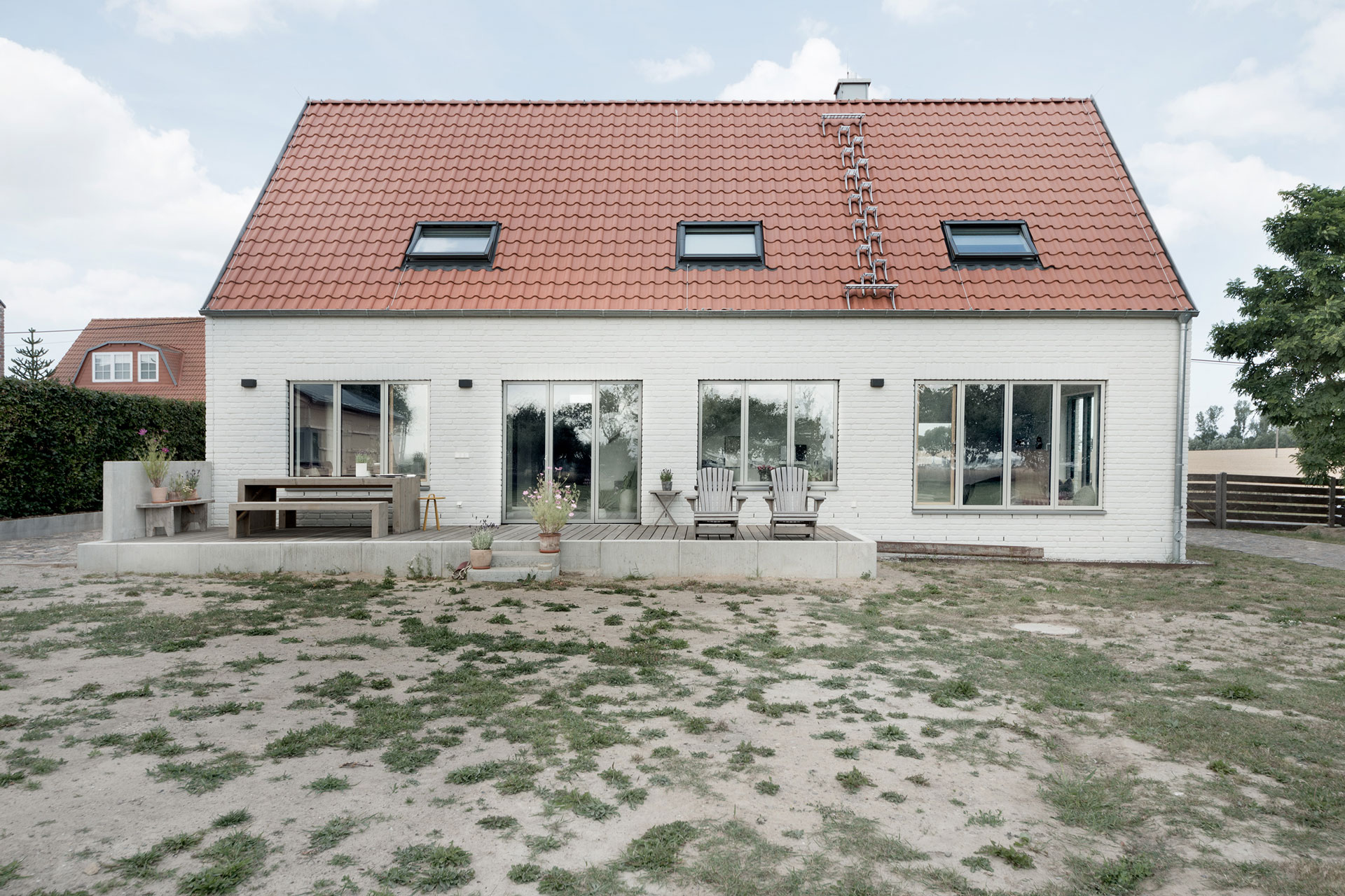 Auf einer großzügigen Holzterrasse stehen zwei Bänke, ein Tisch, zwei Stühle und Blumenkübel.