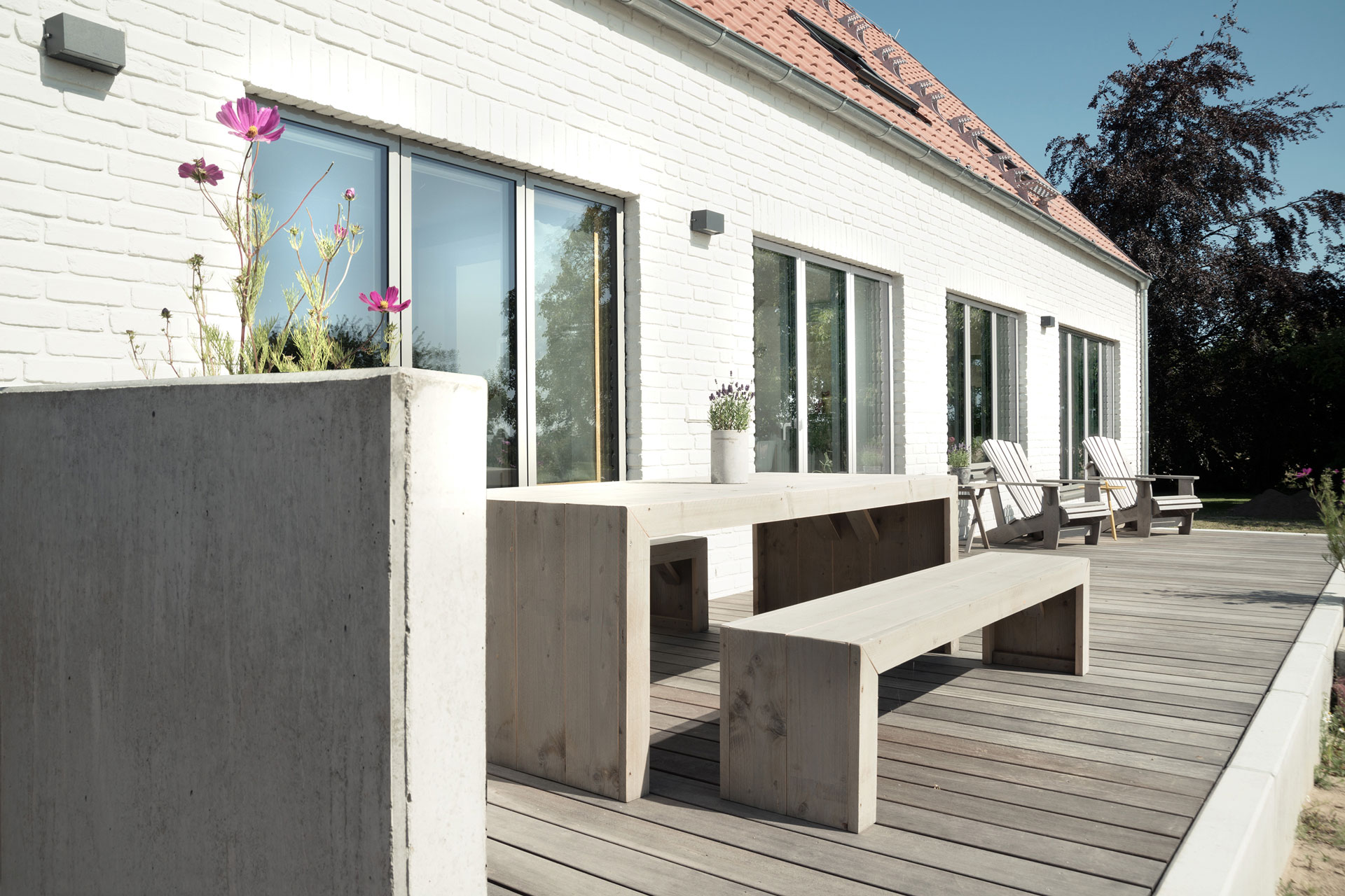 Auf einer Holzterrasse sind zwei lange Bänke und ein Tisch aus massivem Holz.