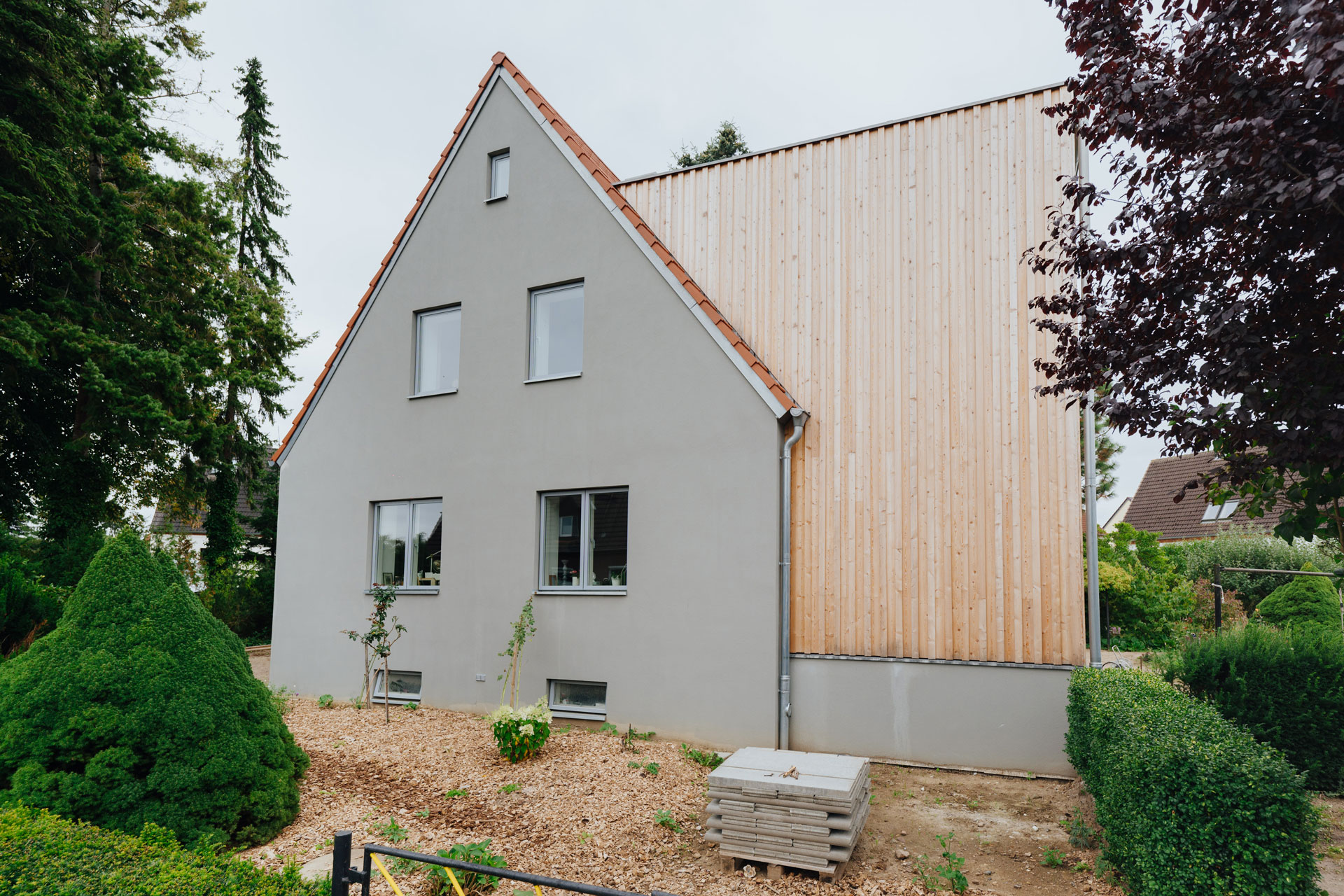 Einfamilienhaus hat einen großen Holzanbau. Die Fassade ist hellbrau.