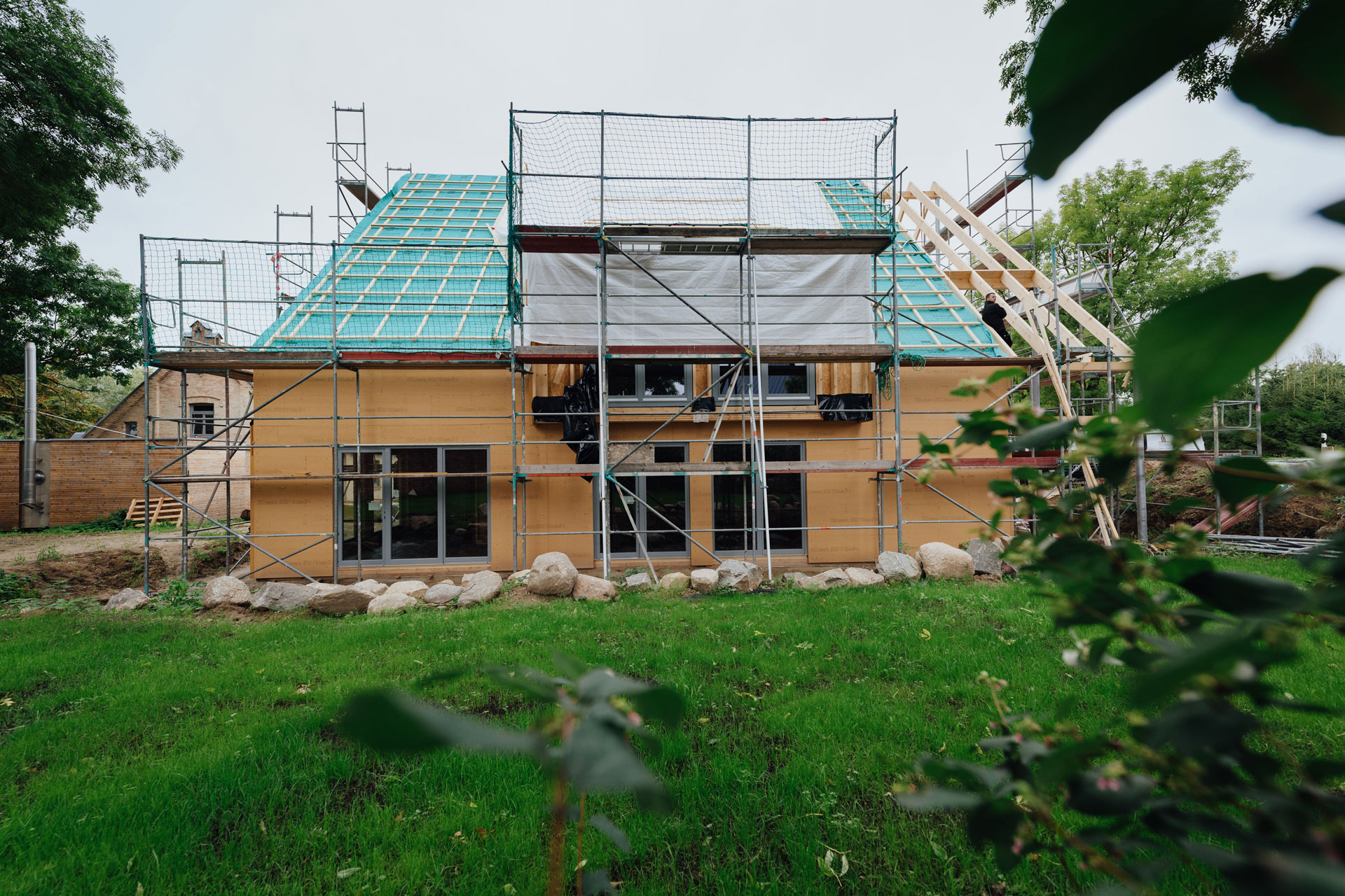 Ein Mehrfamilienhaus ist komplett eingerüstet. Ein großer grüner Baum steht hinter dem Haus.