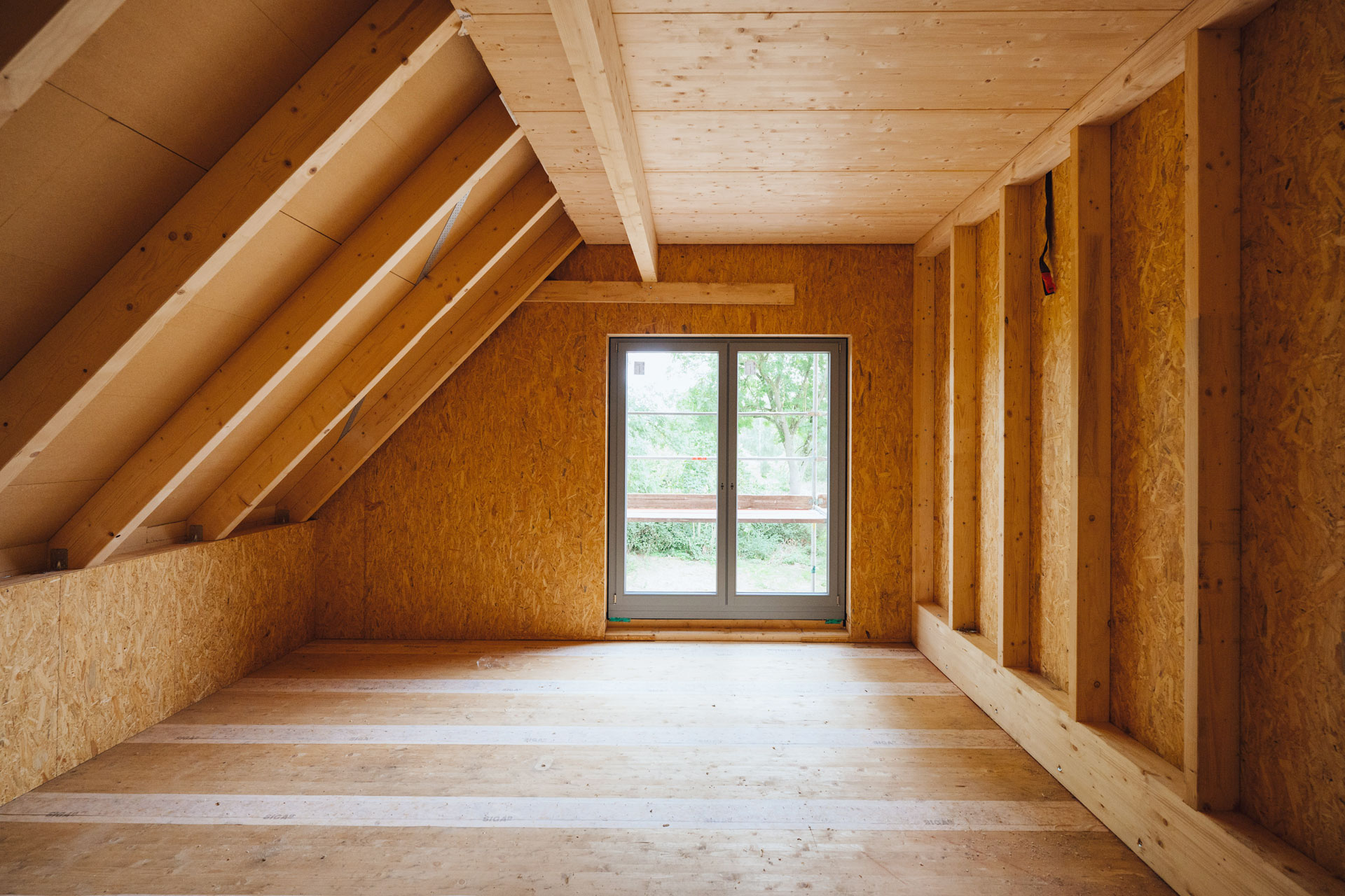Die Holzkonstruktion im Dachgeschoß des Mehrfamilienhauses wirkt massiv. Licht fällt durch eine Terrassentür ein.