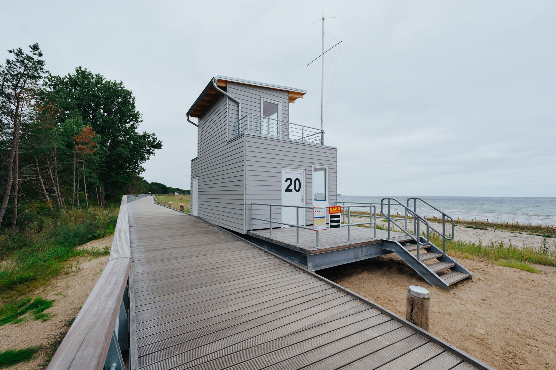 Ein Strandhaus im hellem Grau ist rückseitig zu sehen. Dahinter ist die Ostsee.
