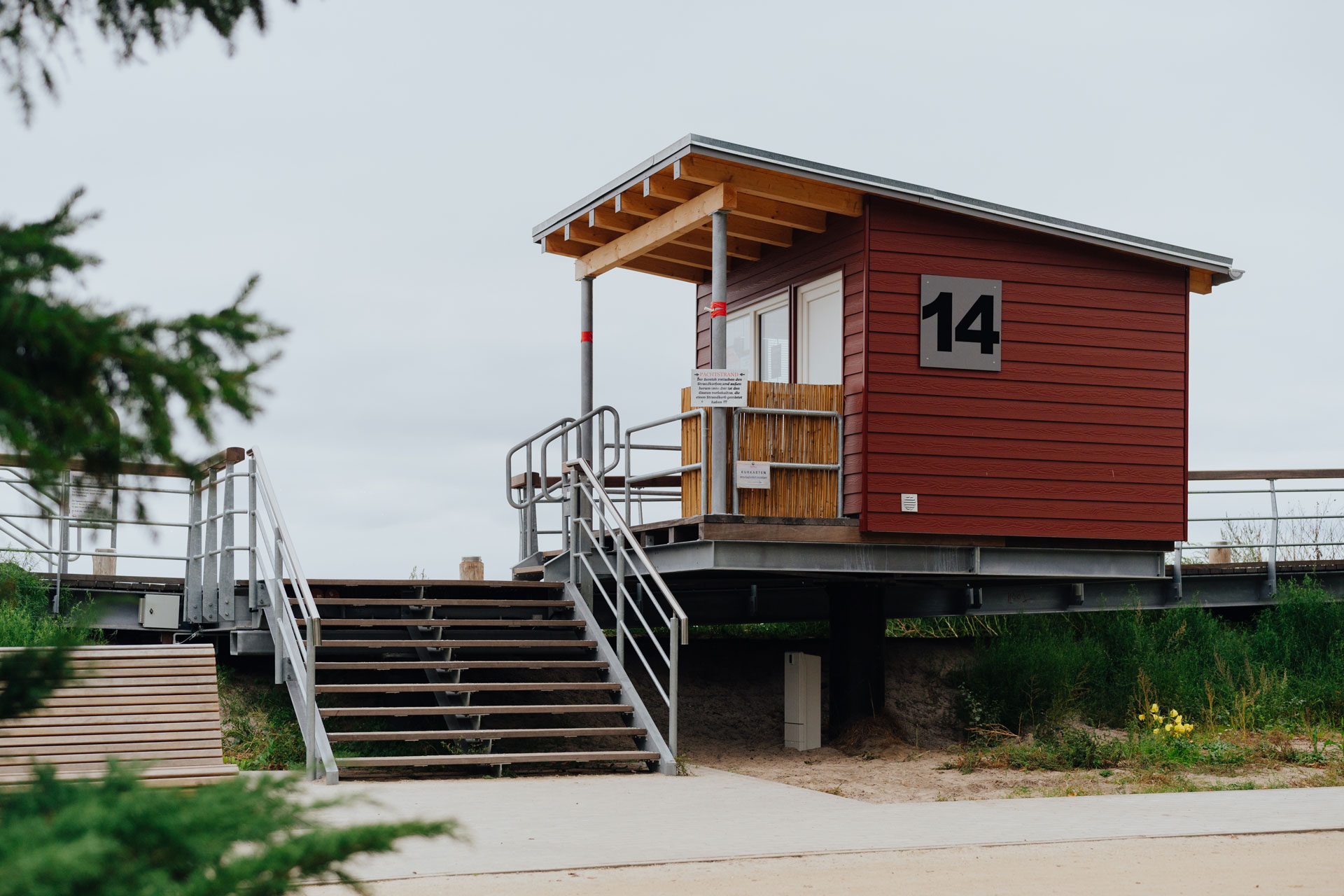 An einem Strandhaus mit braunrot gestrichenen Holz steht die Nummer 14 auf einem Schild.