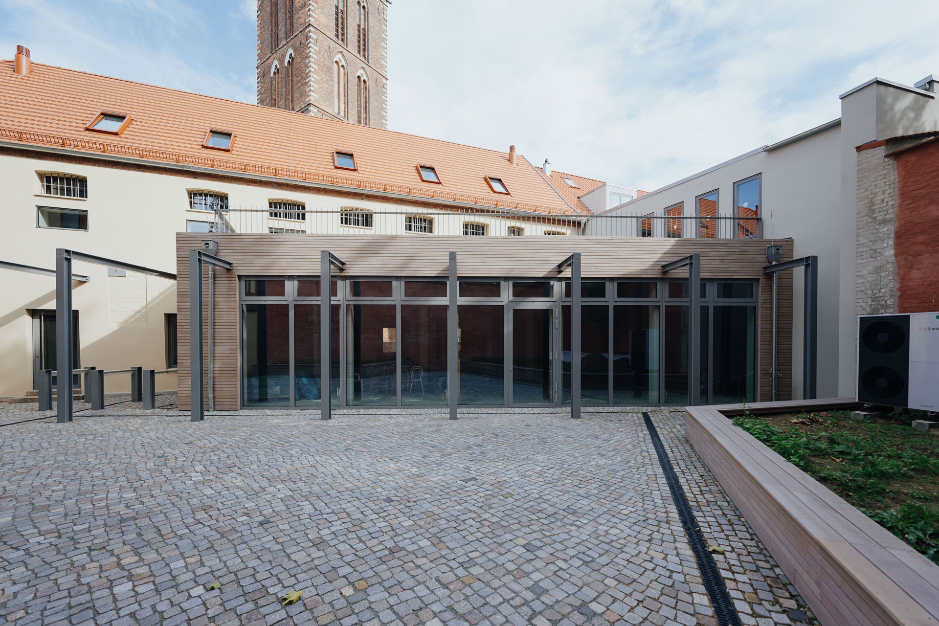 Im Innenhof einer Beherbergungsstätte blickt man auf einen Holzanbau mit darüber befindlicher Terrasse.