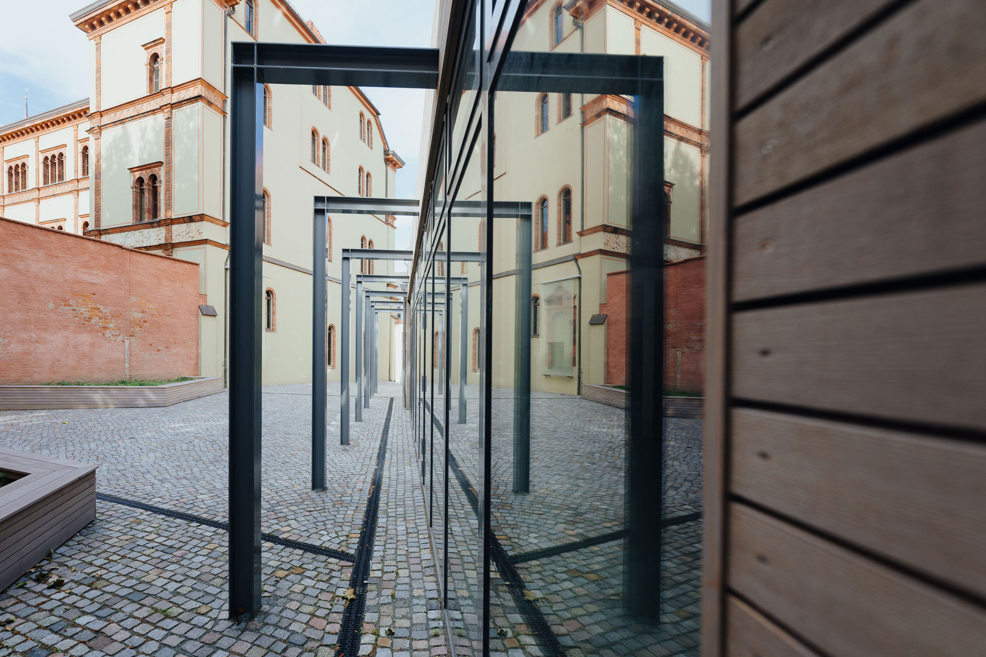 In den Glasscheiben des Holzanbaus spiegelt sich ein gegenüberliegendes Gebäude.