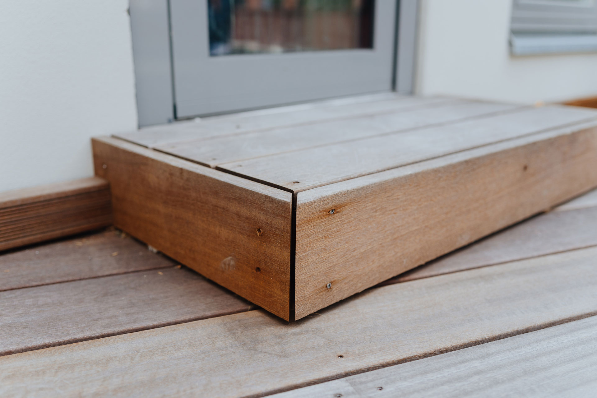 Vom Terrassenboden aus Holz ist ein Übergang mit Holzstufe zu einer Tür.