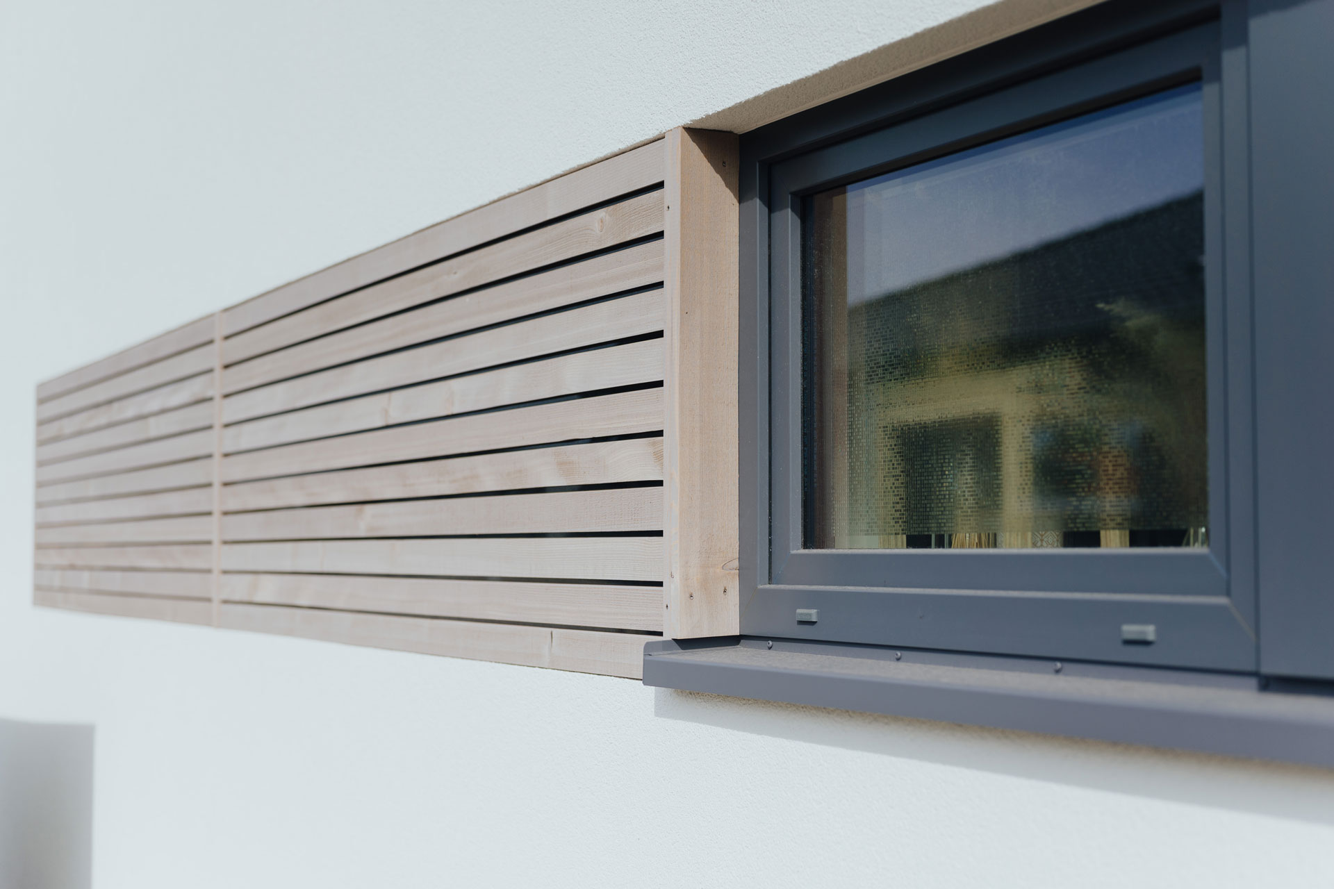 Ein kleines eckiges Fenster hat eine seitliche Holzverkleidung auf einer sonst weißen Fassade.