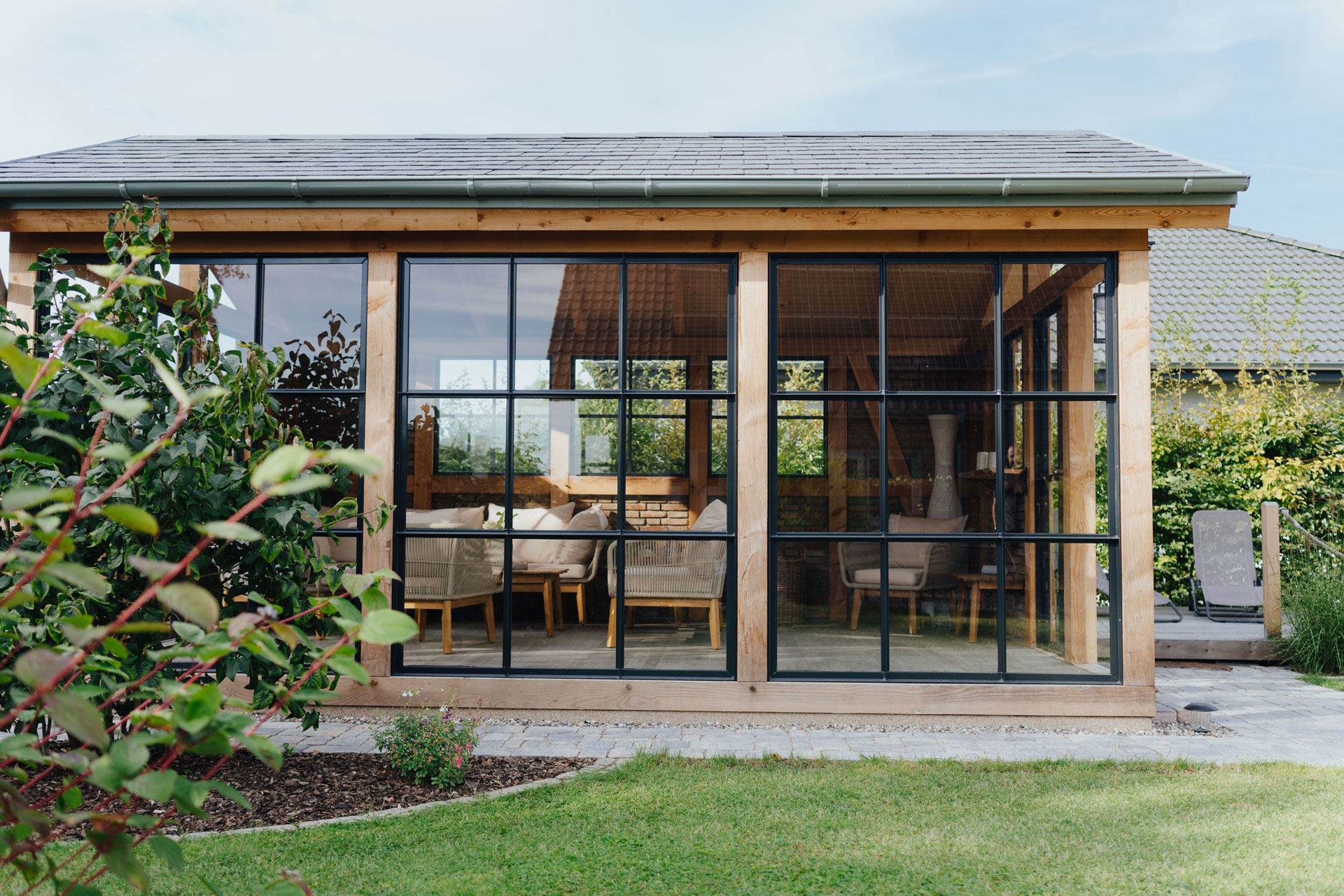 Durch die großen Fenster des Gartenhauses kann man in den wohnlich eingerichteten Innenraum sehen.