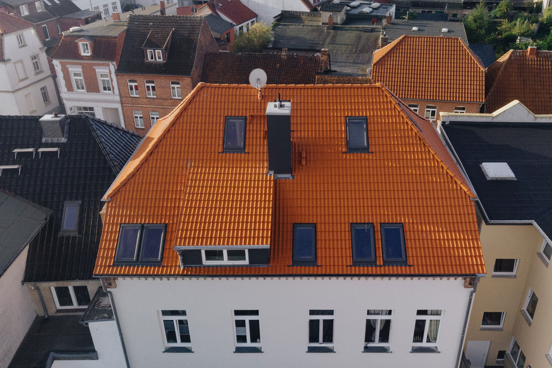 Das rote Ziegeldach eines Mehrfamilienhauses grenzt neben zwei andere an.