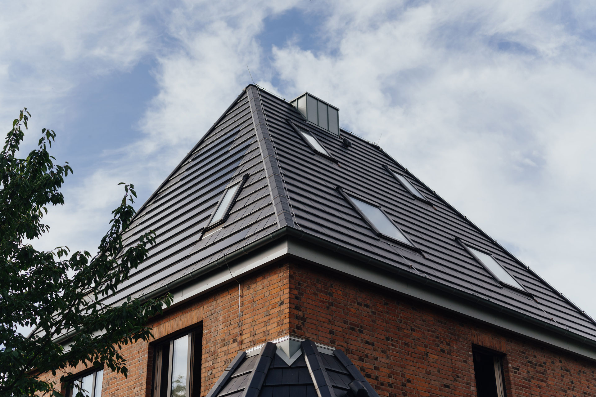Die Solardachziegel eines Hauses glänzen in der Sonne. Der Himmel ist leicht bewölkt.