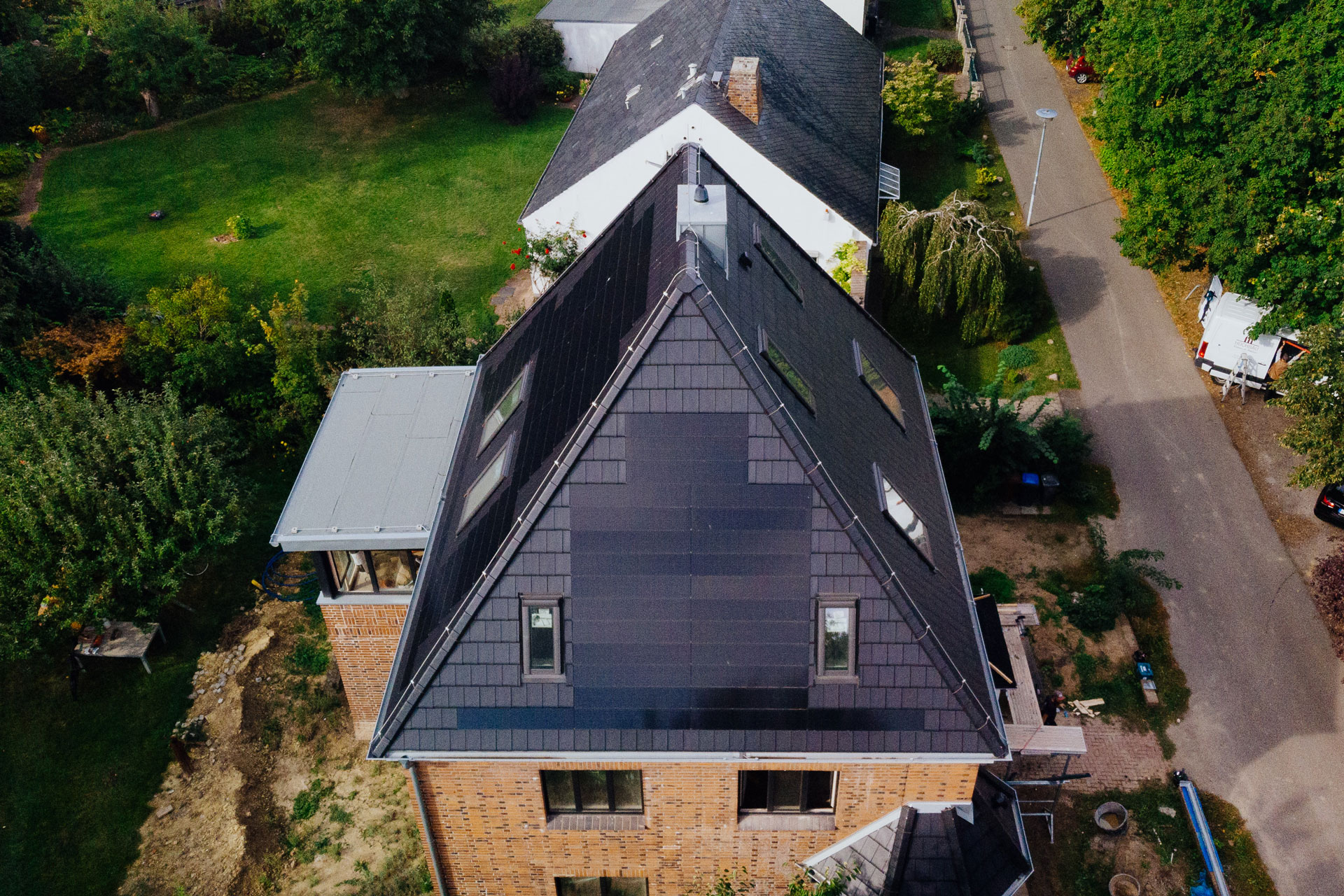 Auf einem freistehenden Einfamilienhaus sind neben schiefergrauen Dachziegeln schwarze Solardachziegel auf dem Dach.