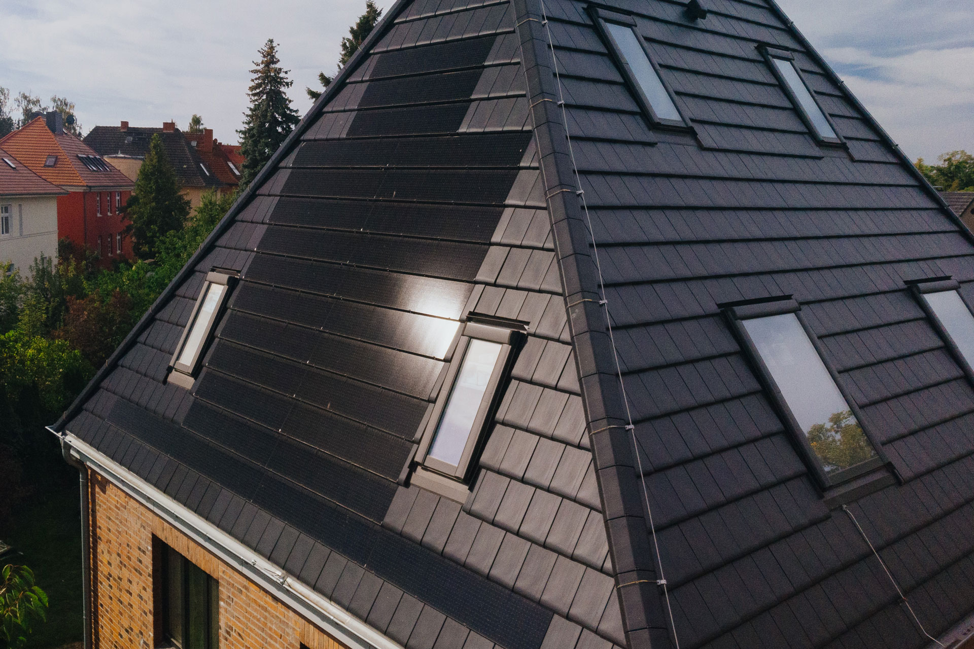 Schwarze Solardachziegel glänzen auf einem Dach mit schiefergrauen Dachziegeln in der Sonne.