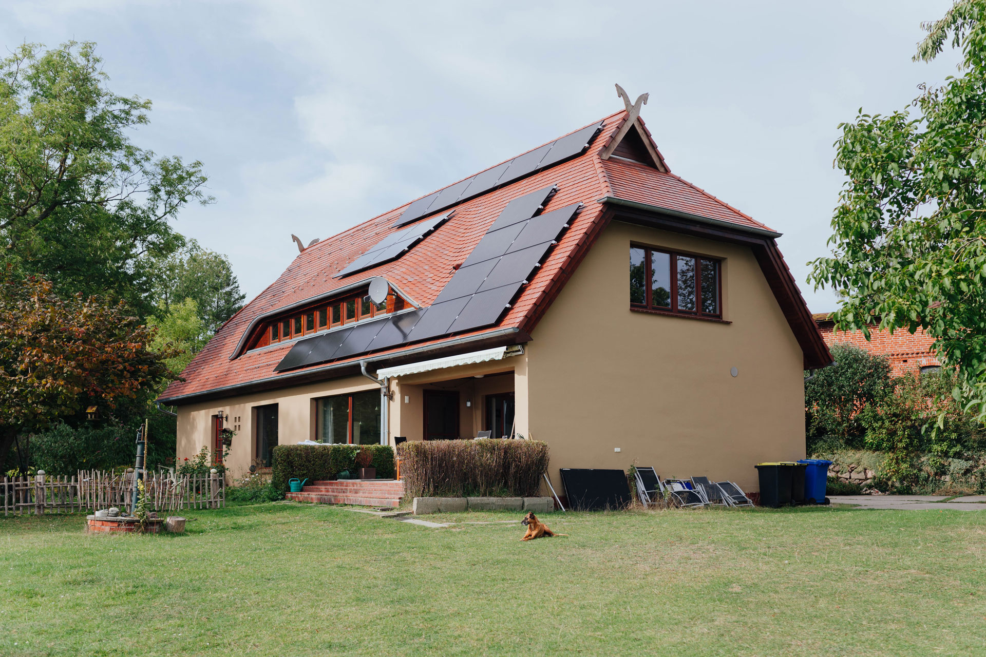 Ein Einfamilienhaus ist idyllisch gelegen. Auf dem Dach glänzen schwarze Solarplatten in der Sonne.