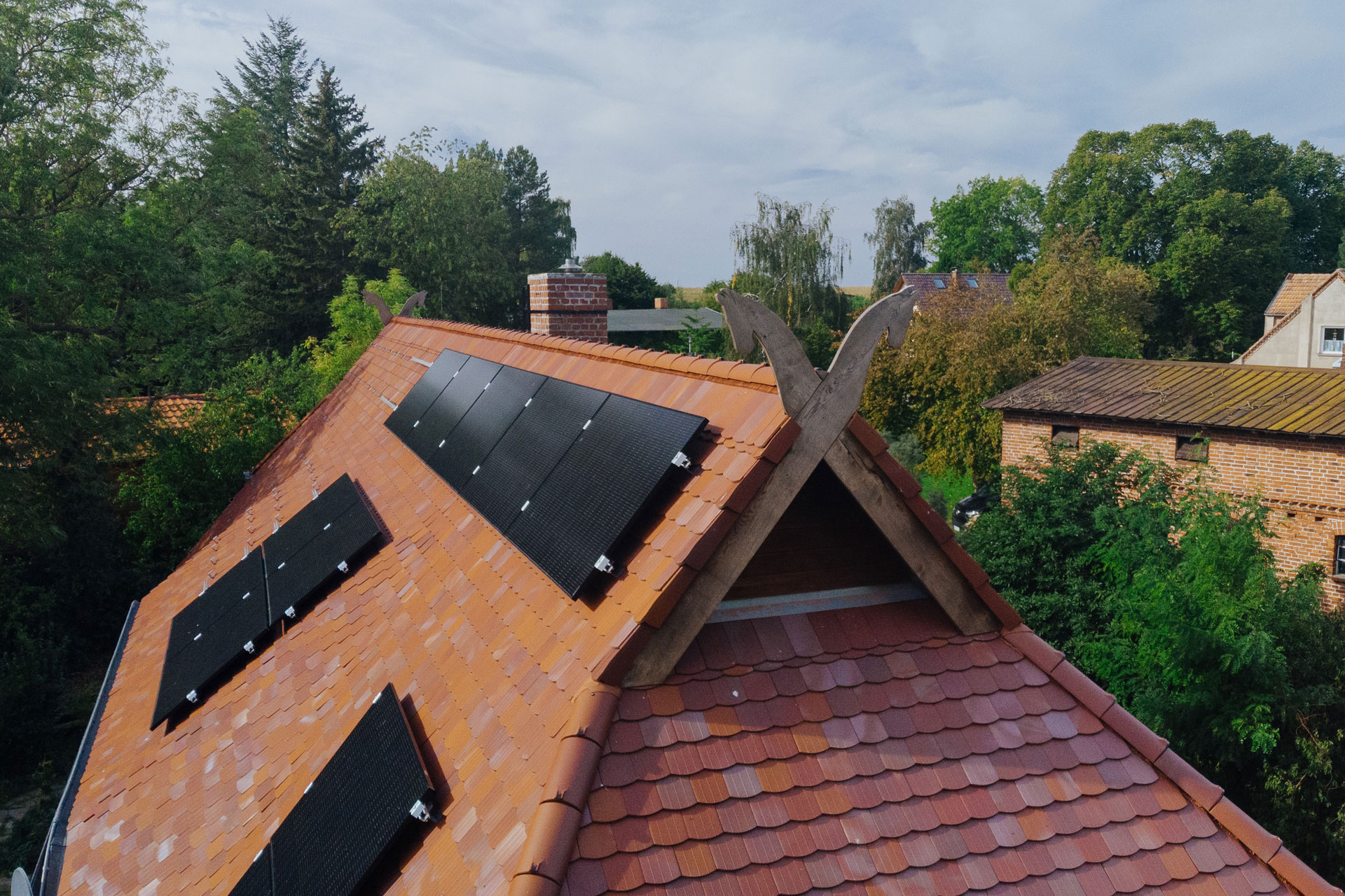Schwarze Solarplatten glänzen in der Sonne. Der Giebelschmuck – gekreuzte Pferdeköpfe – sind auch im Bildausschnitt.