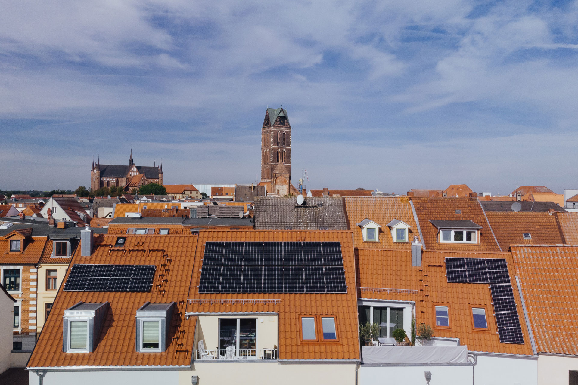 Das rote Ziegeldach mit Solarplatten eines Mehrfamilienhauses ist direkt darüber aus der Vogelperspektive aufgenommen.