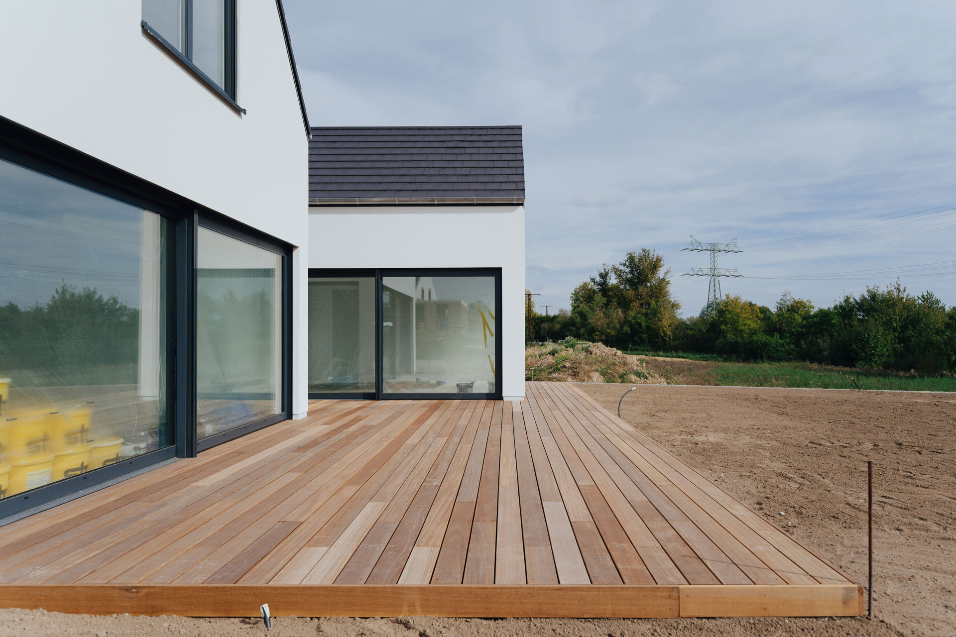 Ein Einfamilienhaus hat einen großzügige Holzterrasse. Im Hintergrund ist ein Feld.